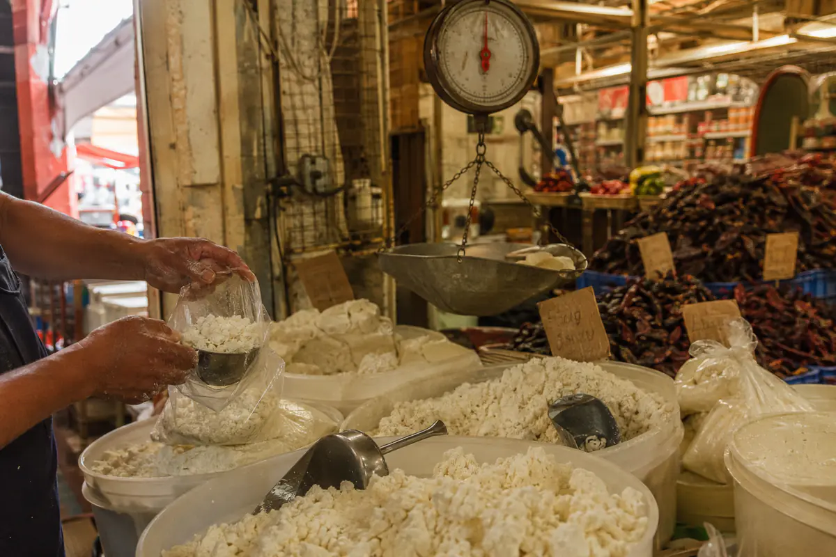 Mostrador de queso a granel en un mercado público mexicano, con báscula y tinas de queso seco desmoronado