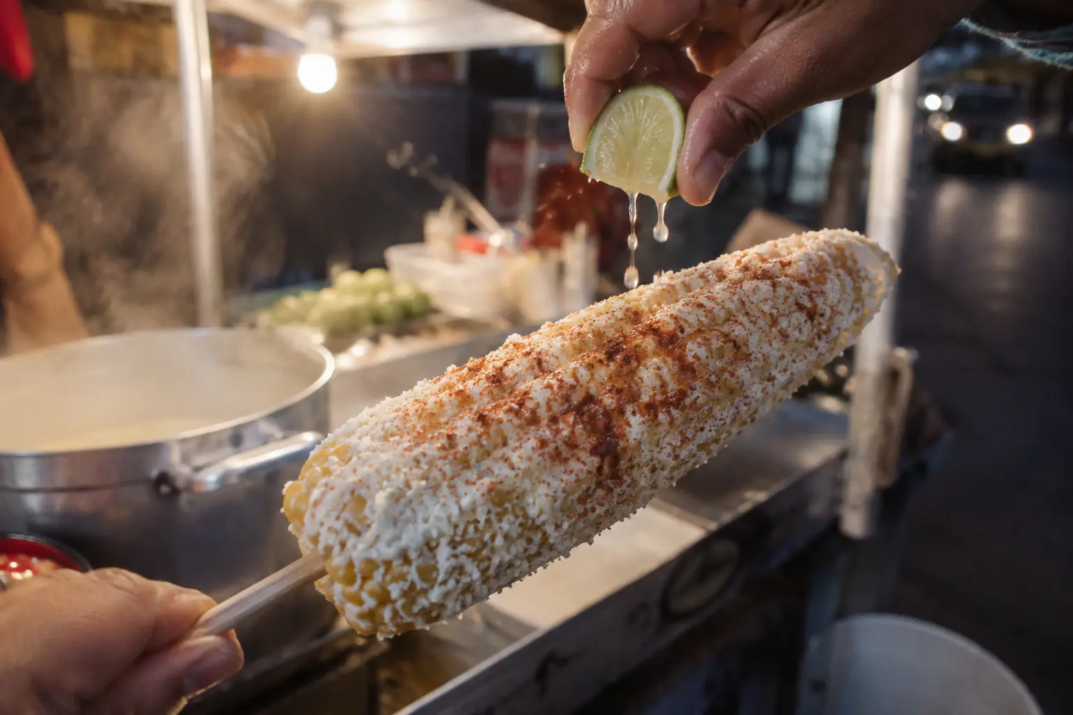 Elote entero preparado con mayonesa, queso elotero análogo y chile en polvo en un carrito de elotes